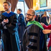 Faculty waiting and getting help with gown